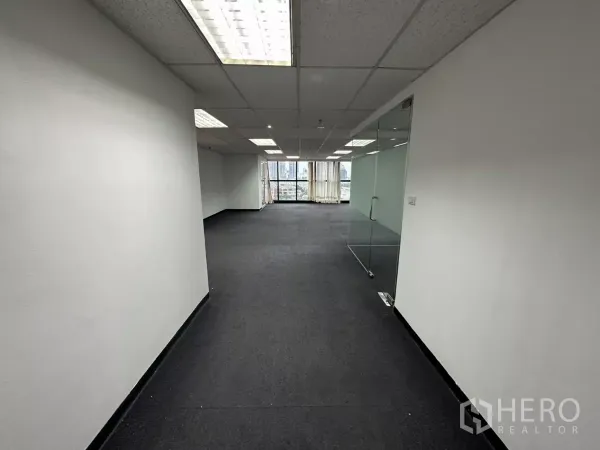 办公空间 出租在Watthana, Bangkok - 入口处望向开放式办公室，地毯地面、格栅吊顶灯，右侧玻璃隔间与城市景观窗。