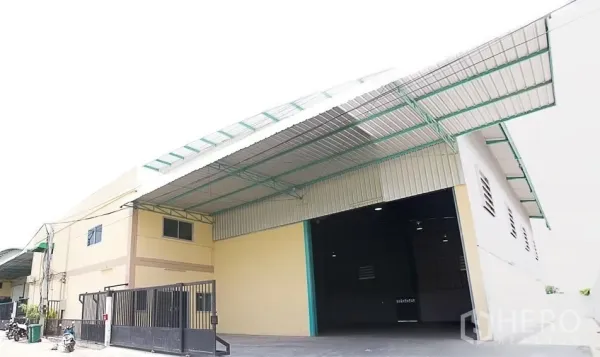 Warehouse for rent in Pathum Thani - Warehouse exterior with wide rolling shutter, large covered loading canopy and secure front gate.