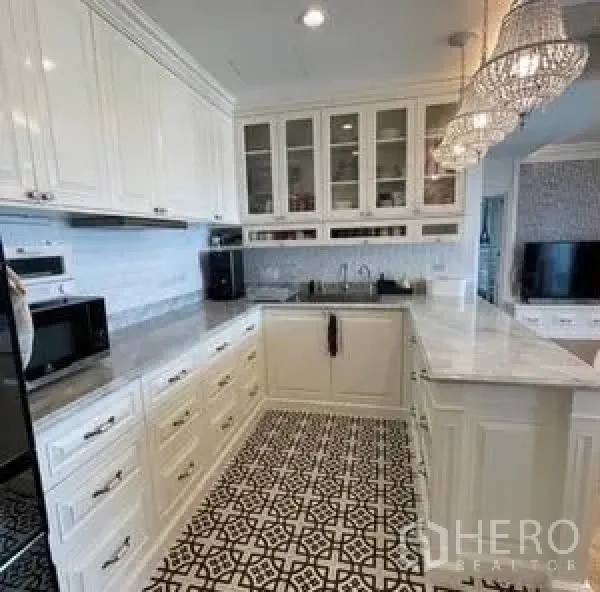 Condominium for rent or sale - U-shaped white kitchen with marble countertops, glass-front cabinets, patterned tile floor, and pendant lights.