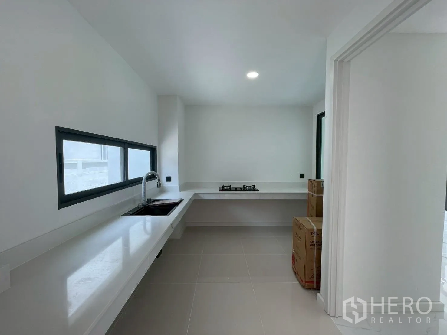 Detached House for sale in Chatuchak, Bangkok - Minimalist kitchen with long white counters, sink, gas cooktop, and windows.