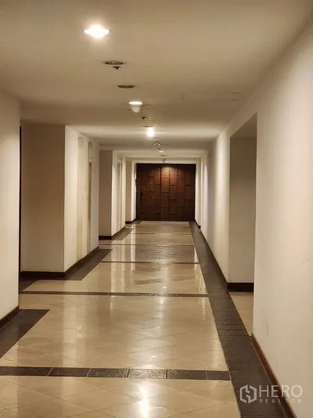 Condominium for rent in Bang Rak, Bangkok - Well-lit condominium corridor with tiled walkway leading to dark wooden entry doors.
