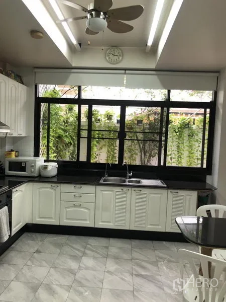ทาวน์เฮาส์ ให้เช่าหรือขายในBangkok - ครัวสว่างตา ตู้สีขาว เคาน์เตอร์หินสีดำ หน้าต่างบานใหญ่เห็นเถาวัลย์ และพัดลมเพดาน