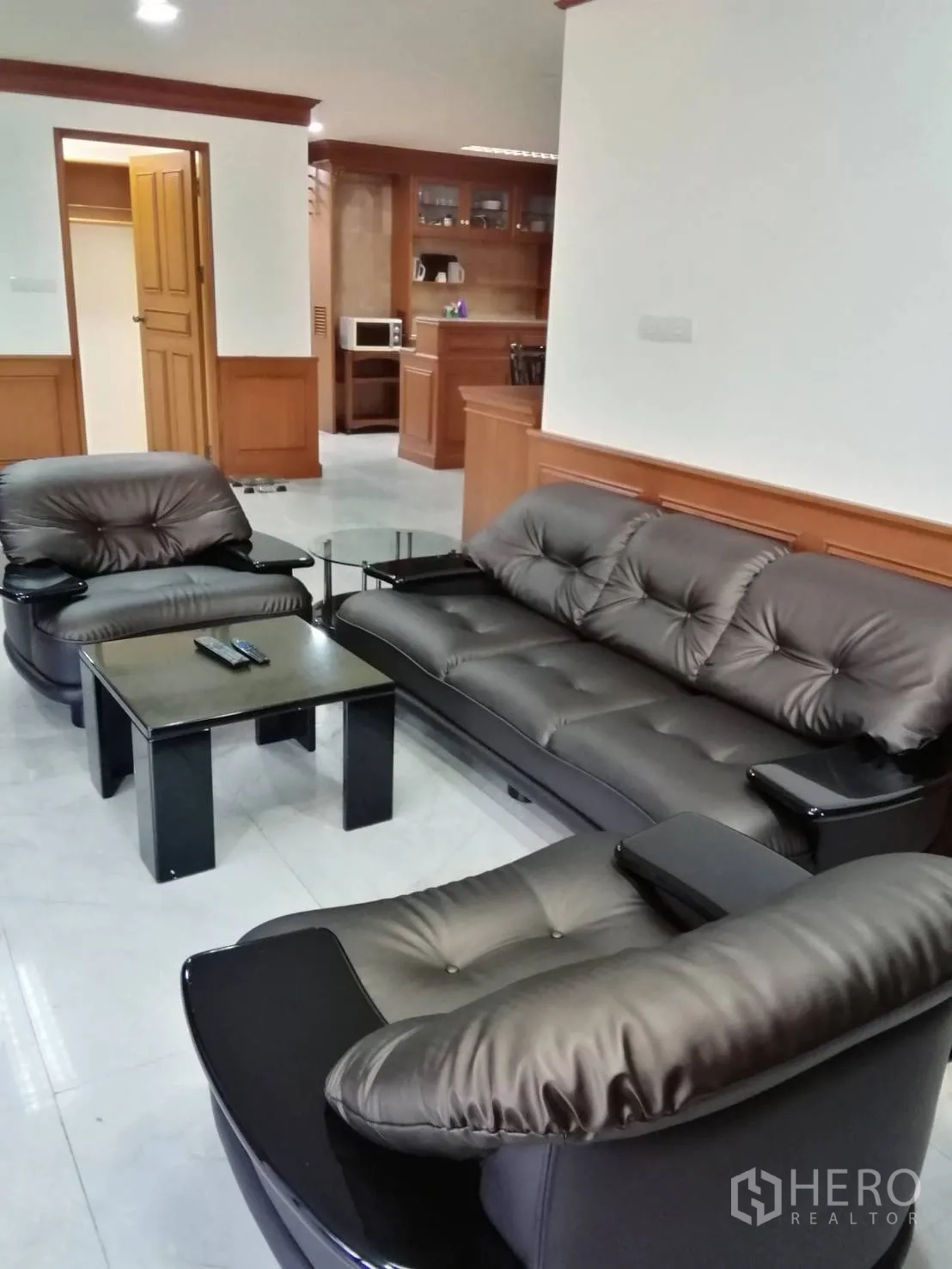 คอนโด ให้เช่าหรือขายในWatthana, Bangkok - มุมนั่งเล่นพร้อมโซฟาหนังและโต๊ะกลางสีดำบนพื้นกระเบื้องเงา