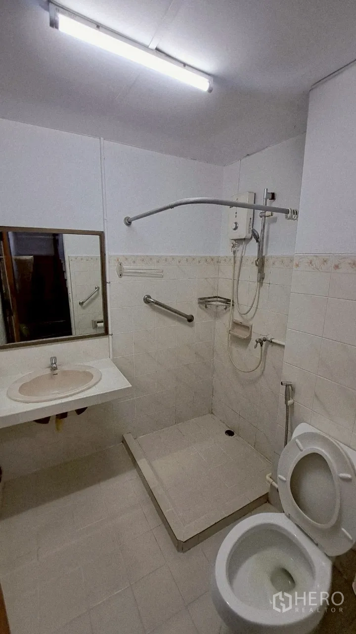 Townhouse for rent in Watthana, Bangkok - Compact bathroom with skylight, handheld shower and white basin.