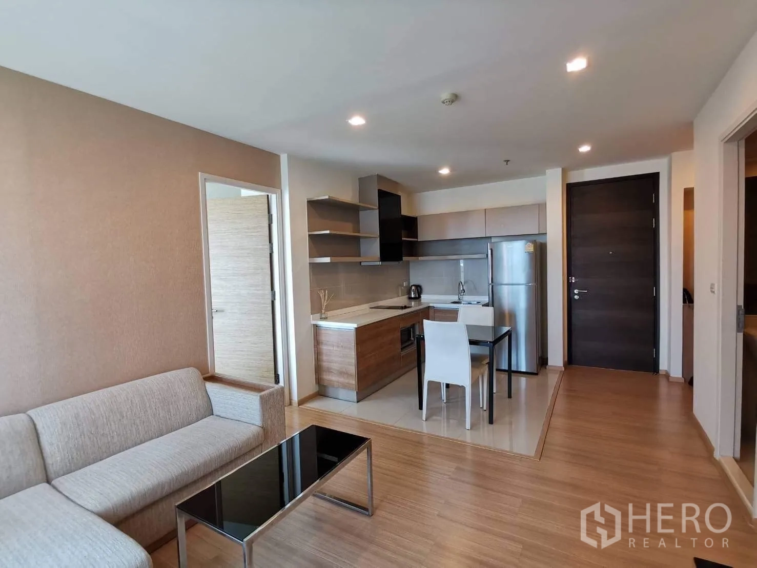 公寓 出租或出售在Khlong Toei, Bangkok - 开放式客厅，浅色转角沙发、黑色玻璃茶几与一体化厨房冰箱。