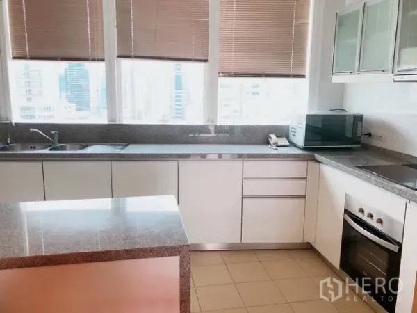 Condominium for rent or sale in Khlong Toei, Bangkok - Modern white kitchen corner with L-shaped counters, stone worktops, cooktop and city views through wide windows.
