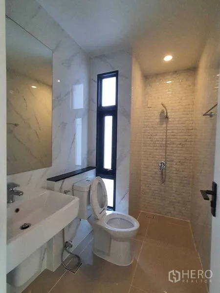 Detached House for sale in Prawet, Bangkok - Compact bathroom with window, sink, toilet, and tiled shower alcove.
