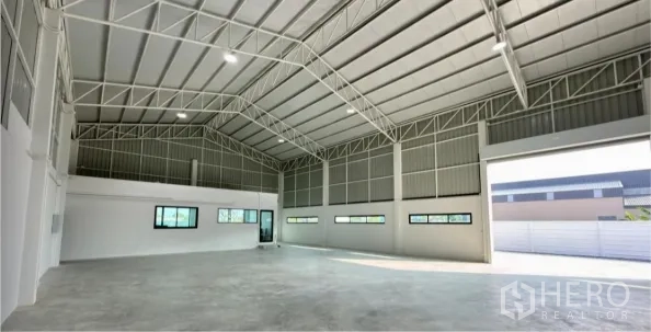 Warehouse for sale in Bang Bua Thong, Nonthaburi - Spacious warehouse interior with high steel truss roof, concrete floor, windows and a wide access door.