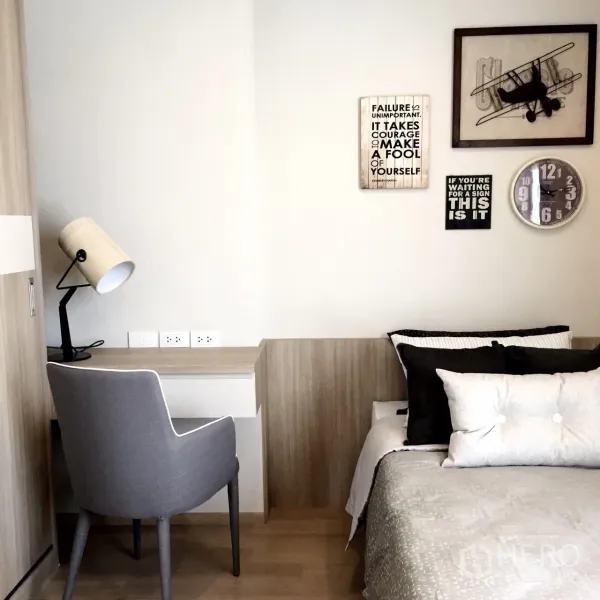 Condominium for rent or sale in Watthana, Bangkok - Secondary bedroom with built‑in study desk, grey chair, wall art and a clock beside a neatly made bed.
