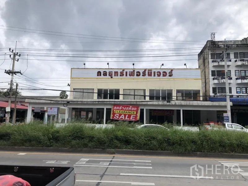 Retail Space for rent in Lam Luk Ka, Pathum Thani - Street view of a two‑storey retail building with a large clearance sale banner and wide main‑road frontage under cloudy skies.