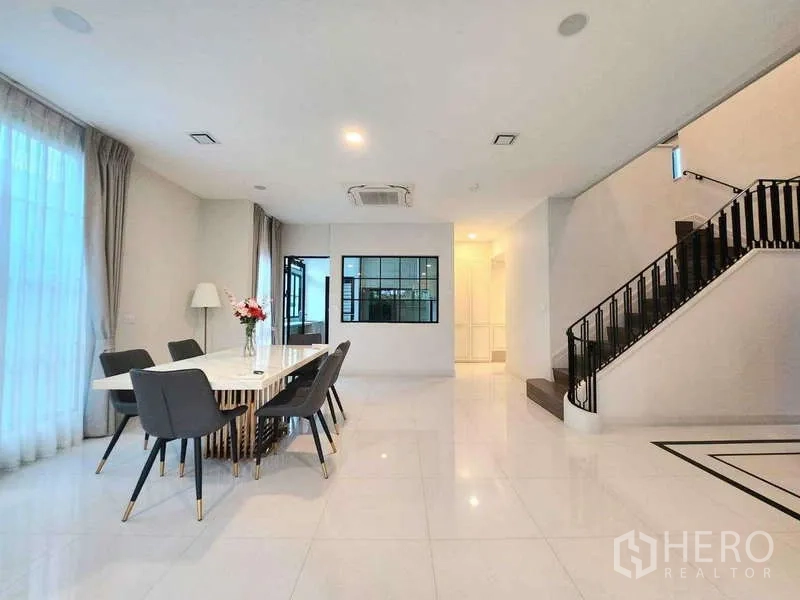 Detached House for rent in Saphan Sung, Bangkok - Dining space adjacent to staircase and large windows, minimalist design with soft lighting.