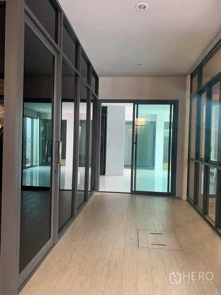 Townhouse for rent or sale in Yan Nawa, Bangkok - Interior corridor with floor-to-ceiling glass partitions and wood-look tiles.
