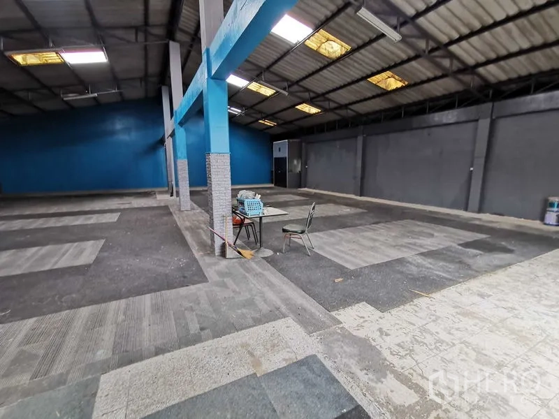 货栈 出租在Nonthaburi - 开放仓库地面，蓝色立柱、灰墙，中间摆放小桌椅。