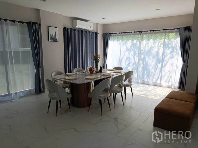 Detached House for rent in Bueng Kum, Bangkok - Dining room with six-seat table, wraparound windows, and sheer curtains letting in daylight.