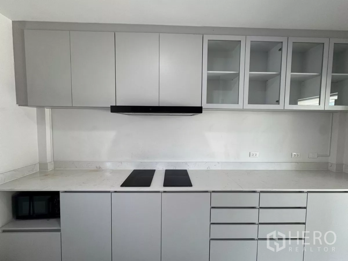 Detached House for rent in Bang Phli, Samut Prakan - Minimal white kitchen with induction hob, hood and ample overhead cabinets.