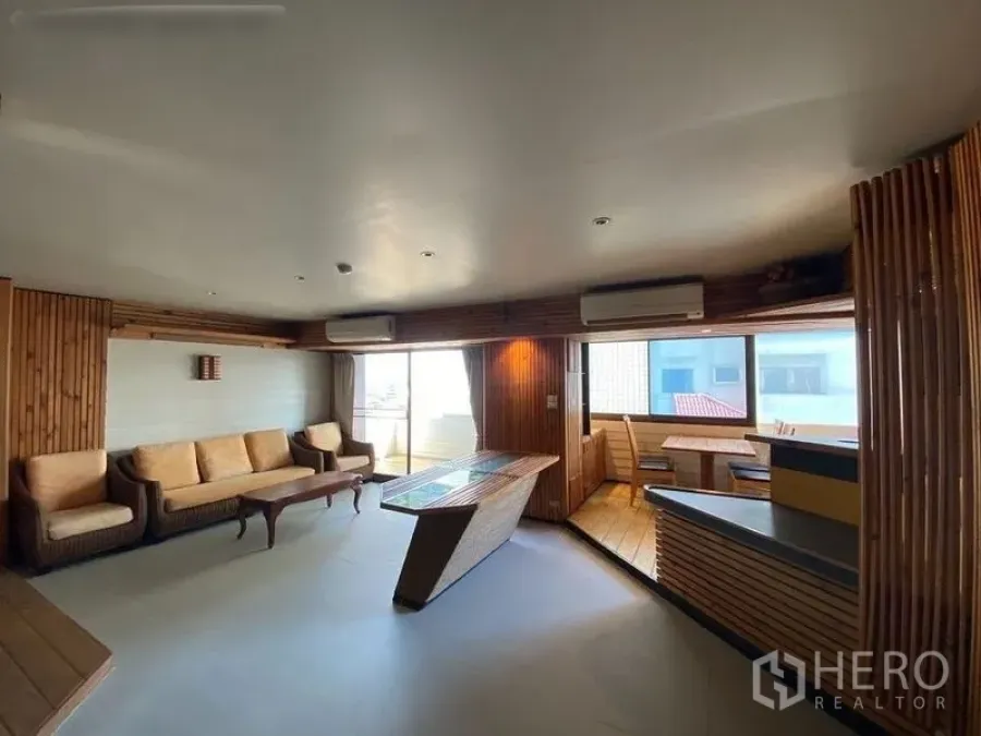 Condominium for rent or sale in Suan Luang, Bangkok - Spacious living room with wood paneling, sofa set, large windows and balcony access in a Bangkok condo.