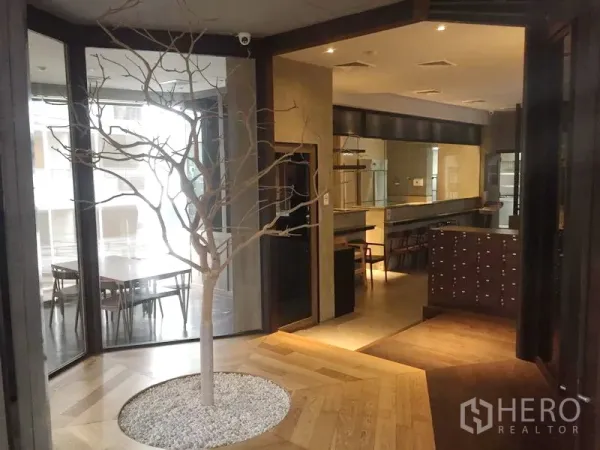 零售空间 出租在Khlong Toei, Bangkok - 入口前厅带玻璃隔断与装饰性室内树，旁设座位区