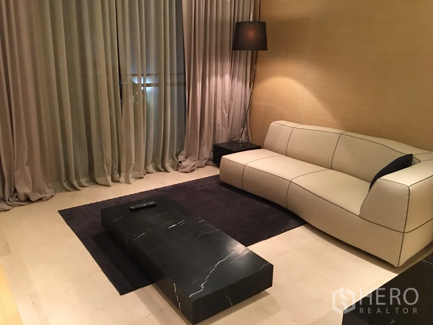 公寓 出租或出售在Bang Rak, Bangkok - 现代客厅，米色沙发、黑色大理石茶几与落地灯。