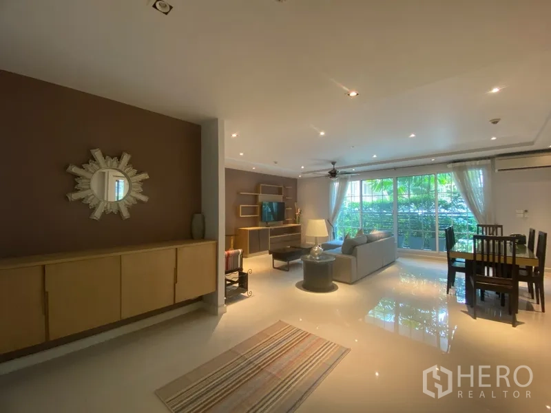 Apartment for rent in Pathum Wan, Bangkok - Open-plan living and dining area with large windows, garden view and built-in TV wall unit.