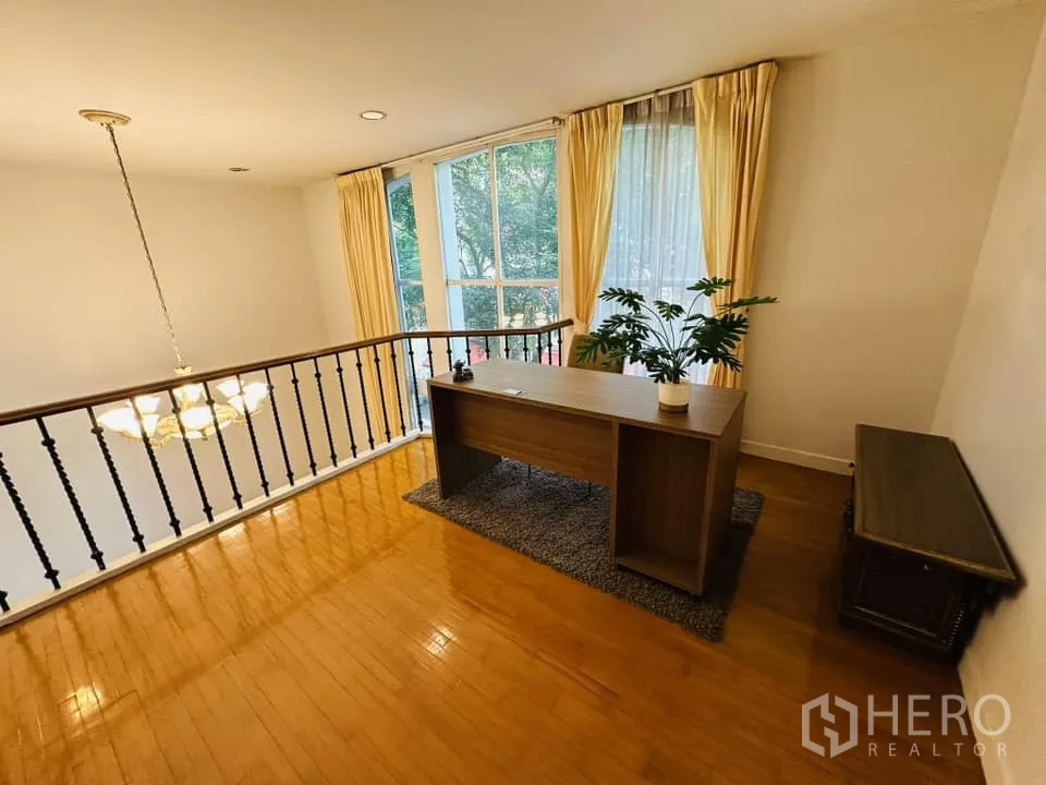 Townhouse for rent in Watthana, Bangkok - Mezzanine home office overlooking the living room, large windows with curtains and a chandelier.