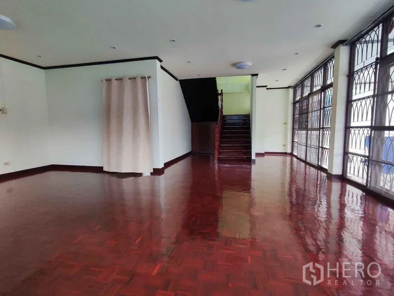 Detached House for rent in Khlong Toei, Bangkok - Large open-plan ground floor with shiny wood flooring, staircase and floor-to-ceiling windows with grilles.
