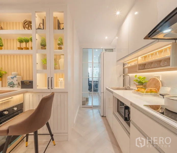 Condominium for sale in Yan Nawa, Bangkok - Galley kitchen looking toward utility room with glass sliding door and tall fridge.