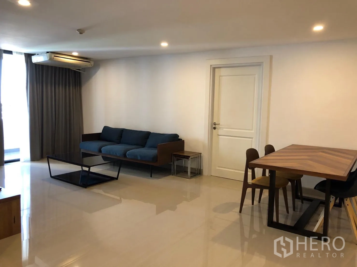 คอนโด ให้เช่าในWatthana, Bangkok - ห้องนั่งเล่นและรับประทานอาหารกว้าง โซฟาสีน้ำเงิน โต๊ะไม้ แอร์ และผ้าม่านสูงจรดพื้น