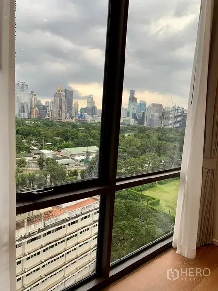 Condominium for rent in Pathum Wan, Bangkok - City skyline and green park view through a large condo window in Bangkok.
