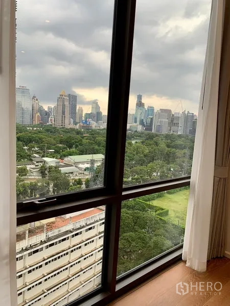 Condominium for rent in Pathum Wan, Bangkok - City skyline and green park view through a large condo window in Bangkok.