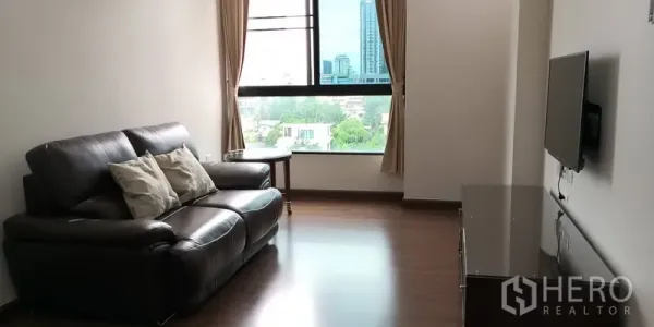 Condominium for rent in Sathon, Bangkok - Bright living room with leather sofa, wall‑mounted TV and large window offering a city view in a Sathon condo.