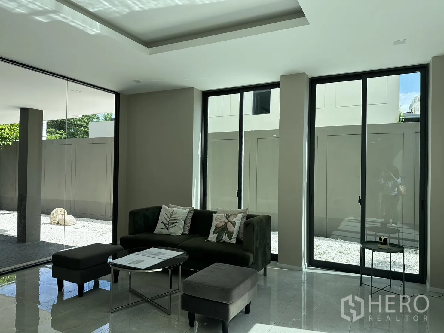 Home Office for rent or sale in Suan Luang, Bangkok - Bright lounge area with dark sofa, ottoman, and floor-to-ceiling windows.