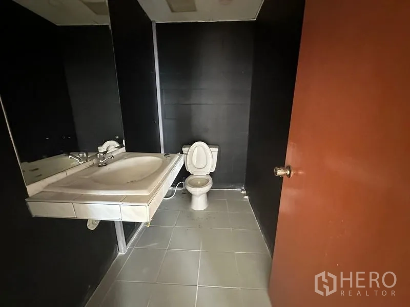 办公空间 出租在Pathum Wan, Bangkok - 套内卫生间，坐便器、大镜面与瓷砖地面。