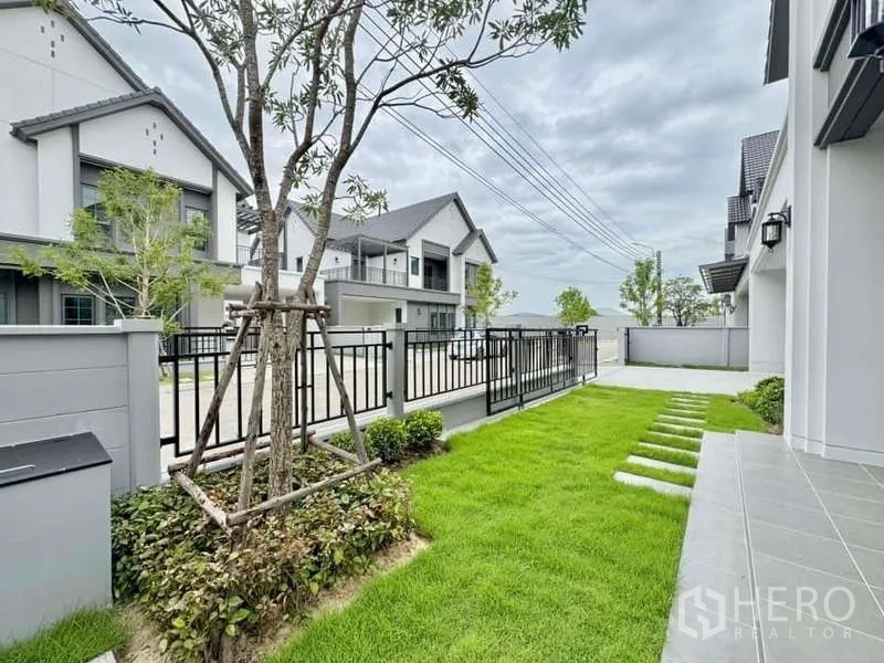 Detached House for sale in Bang Phli, Samut Prakan - Front garden with lawn, young tree and black metal gate.