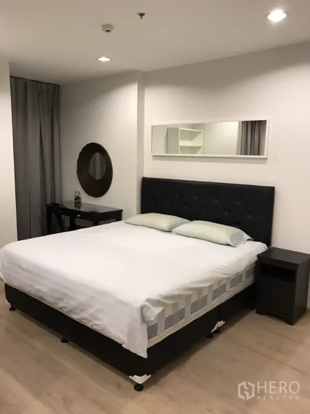 Condominium for rent or sale in Ratchathewi, Bangkok - Bright bedroom with an upholstered bed, long wall mirror, bedside table and light wood flooring.
