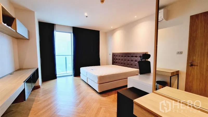 Condominium for sale in Watthana, Bangkok - Bedroom with balcony access, city view, built-in desk and upholstered headboard.