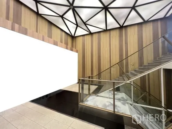 零售空间 出租在Watthana, Bangkok - 商场中庭，几何灯顶、木质墙面与玻璃楼梯扶手。