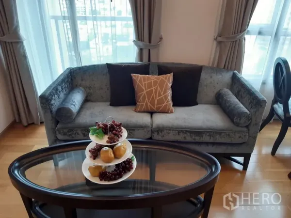คอนโด ให้เช่าในWatthana, Bangkok - โซฟากำมะหยี่สีเทาริมหน้าต่าง พร้อมโต๊ะกลางทรงรีและผลไม้ตกแต่ง