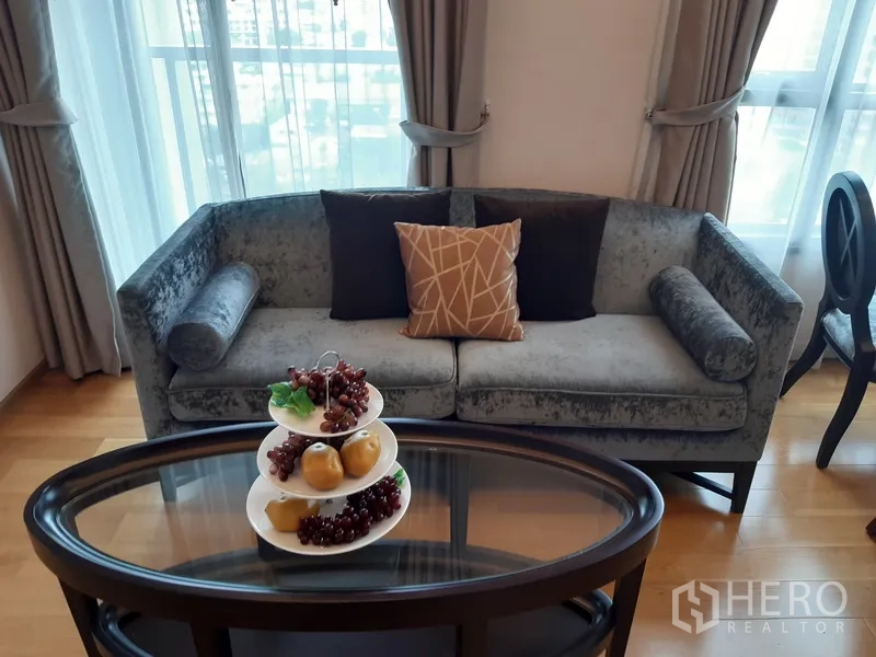 คอนโด ให้เช่าในWatthana, Bangkok - โซฟากำมะหยี่สีเทาริมหน้าต่าง พร้อมโต๊ะกลางทรงรีและผลไม้ตกแต่ง
