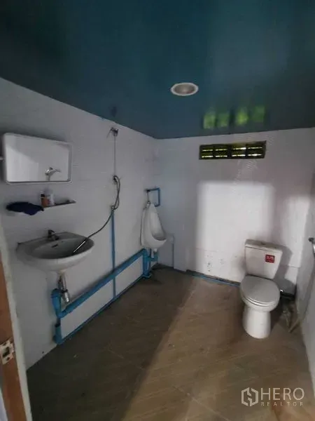 货栈 出租在Nonthaburi - 仓库卫生间，含坐便器、小便池、洗手盆与蓝色天花。