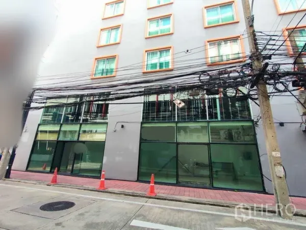 พื้นที่ขายปลีก ให้เช่าในWatthana, Bangkok - หน้าร้านค้าชั้นล่างกระจกเต็มบานใต้ตึกสูงกลาง ทางเท้าปูอิฐสีแดง มีกรวยจราจร และสายไฟเหนือศีรษะ