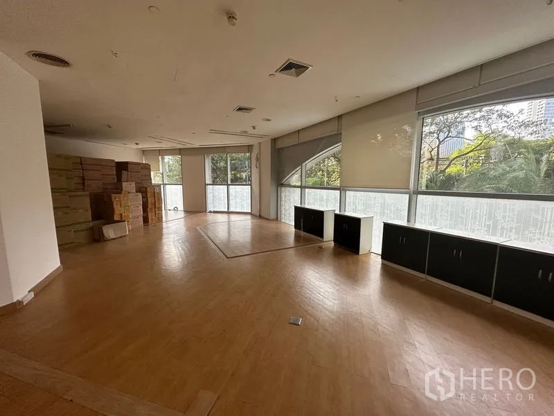 办公空间 出租在Pathum Wan, Bangkok - 大面积办公室，木地板与矮柜，宽窗外是绿树景观。