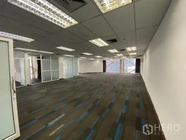 Office Space for rent in Khlong Toei, Bangkok - Long office floor with grid ceiling, AC vents and large cross-braced windows beside frosted glass partitions with city outlook.