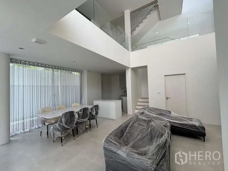 Townhouse for rent or sale in Don Mueang, Bangkok - Double-height living and dining space with large windows and a staircase; furniture wrapped.
