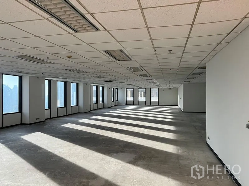 สำนักงาน ให้เช่าในKhlong Toei, Bangkok - พื้นที่สำนักงานแปลนโล่ง รับแสงธรรมชาติ เพดานดรอปไฟฟลูออเรสเซนต์ เงาแสงทอดยาวบนพื้นคอนกรีต และหน้าต่างหลายบานเห็นวิวเมือง