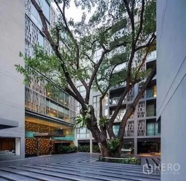 公寓 出售在Watthana, Bangkok - 庭院视角，中央大树与带装饰格栅的阳台立面。