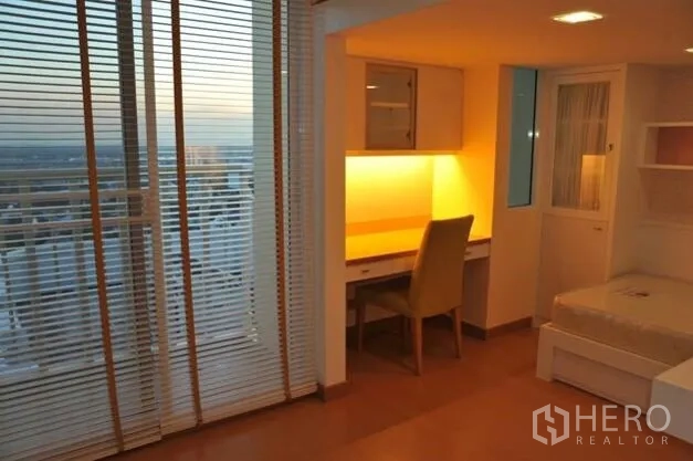 คอนโด ให้เช่าหรือขายในWatthana, Bangkok - มุมห้องนอนพร้อมโต๊ะทำงาน แสงไฟอบอุ่น ม่าน และวิวระเบียงยามเย็น