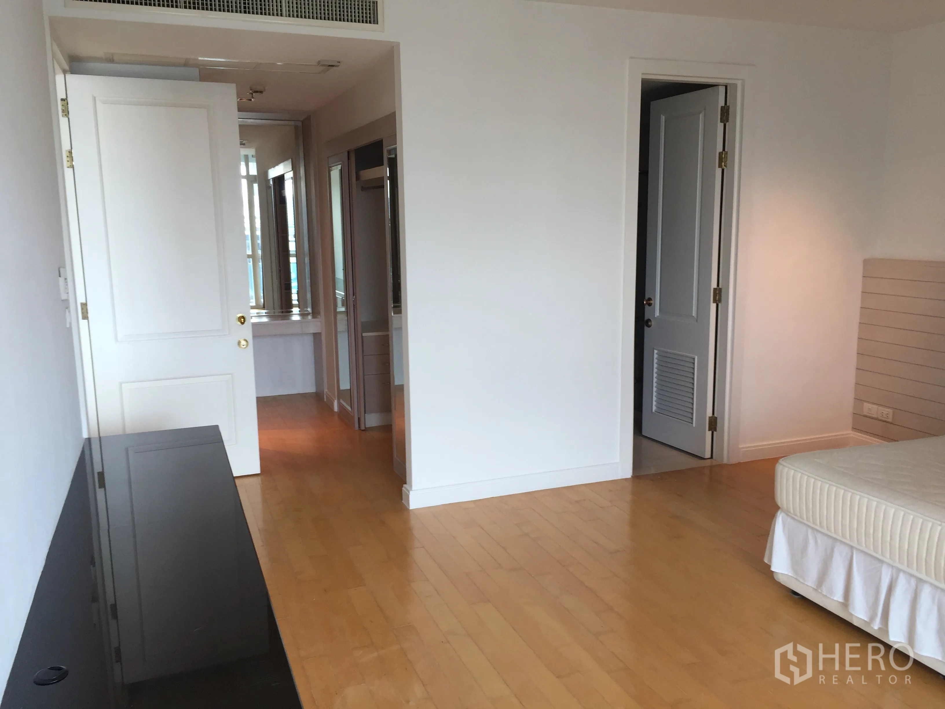 Condominium for rent in Pathum Wan, Bangkok - Master bedroom leading to an ensuite bathroom and closet area with wood flooring.