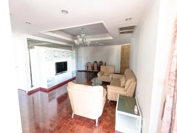 Condominium for rent in Watthana, Bangkok - Spacious lounge with built-in TV unit, detailed ceiling, and dining set on polished wood floors.