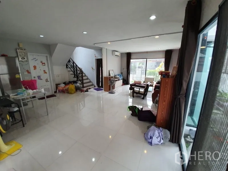 Detached House for sale in Samut Prakan - Living area facing the staircase and front, with large windows and recessed lighting.