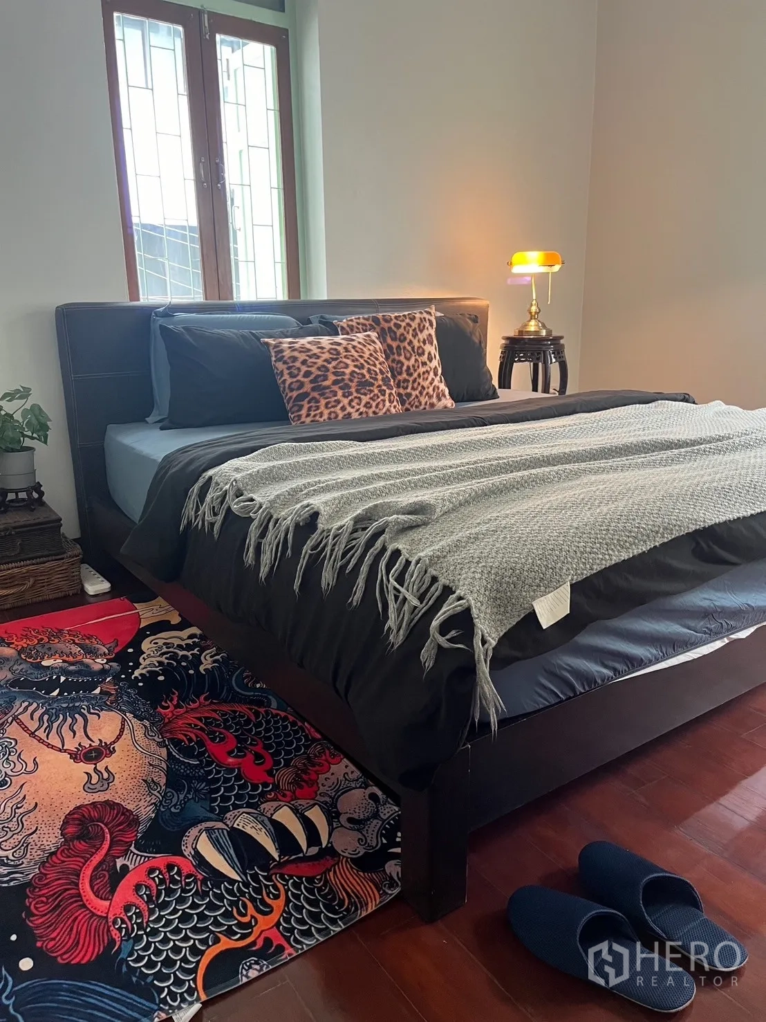 Shophouse for rent in Bang Rak, Bangkok - Bedroom view with bed, patterned rug, and slippers on wood floor.